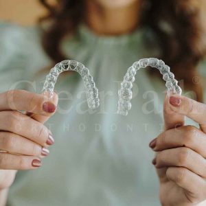 A woman holding a pair of invisible aligners/clear braces up for inspection